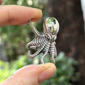 May include: A silver octopus ring with a detailed, textured design. The octopus has eight tentacles and a round head.