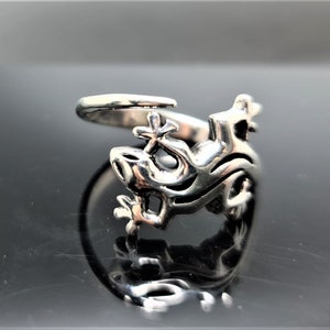 May include: A silver-colored ring featuring a dragon design. The ring has an open design with the dragon's head and body wrapping around the finger. The dragon's features are detailed, with visible eyes, mouth, and scales.
