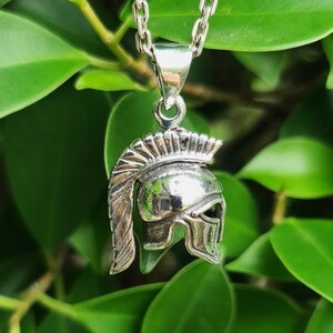 May include: Silver pendant necklace featuring a detailed, three-dimensional design of a Roman soldier's helmet. The helmet has a crested plume and a face guard.
