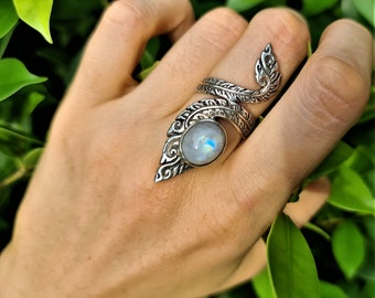 May include: A silver ring with a large, round, iridescent moonstone set in a detailed, leaf-shaped design.