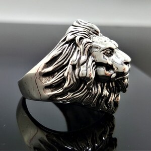 May include: A silver ring with a detailed lion head design. The lion's mane is intricately sculpted and the ring has a polished finish.