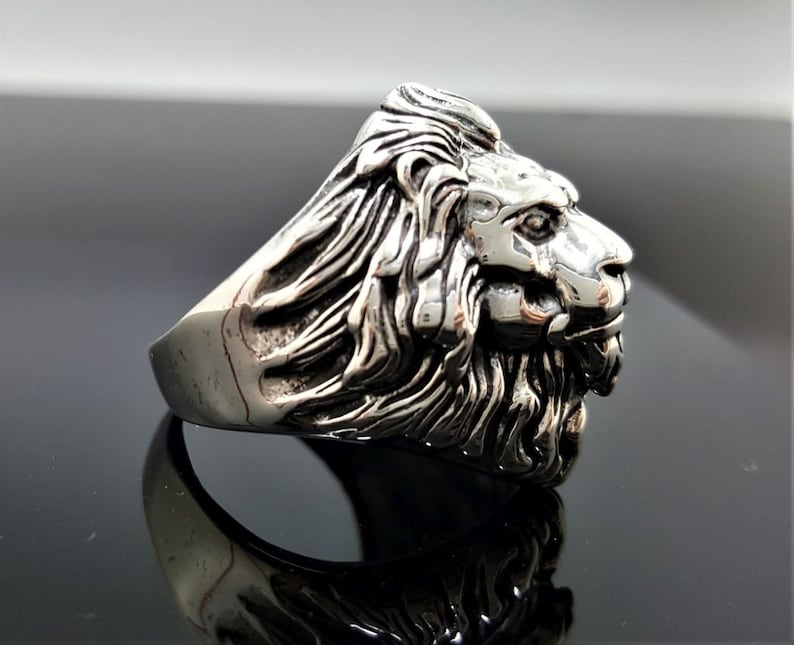 May include: A silver ring with a detailed lion head design. The lion's mane is intricately sculpted and the ring has a polished finish.