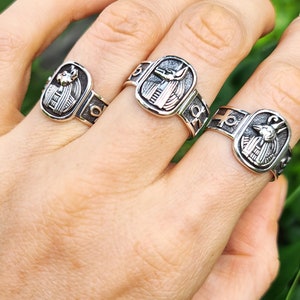 May include: Three silver rings with an Egyptian Anubis design. The rings are worn on a person's fingers.