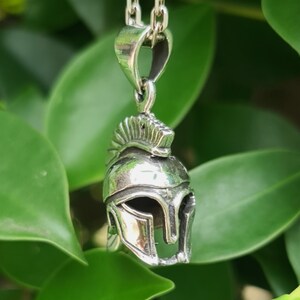 May include: Silver pendant necklace featuring a detailed Spartan helmet design. The helmet is a symbol of strength and courage.