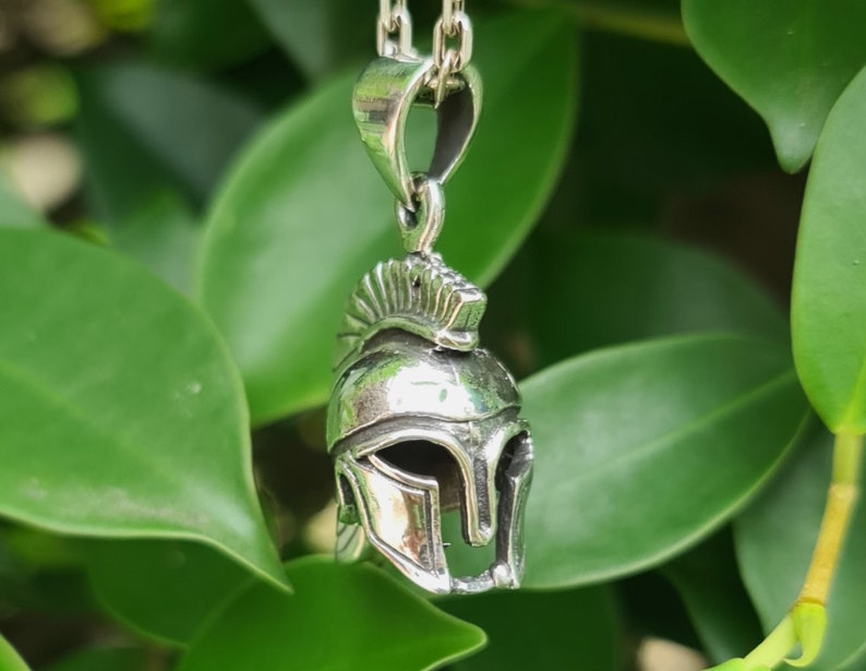 May include: Silver pendant necklace featuring a detailed Spartan helmet design. The helmet is a symbol of strength and courage.