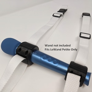 May include: A white strap with black buckles is attached to a blue and black wand holder. The text "Wand not included Fits LeWand Petite Only" is printed on the white surface.