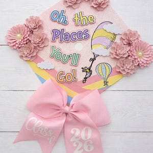 May include: Pink graduation cap decorated with paper flowers and the phrase "Oh, the Places You'll Go!" in colorful lettering. A pink bow with "Class of 2026" is attached. The cap features a Dr. Seuss-inspired illustration.