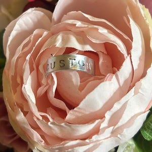 May include: A silver ring with the word "CUSTOM" engraved on it, nestled inside a pink flower.
