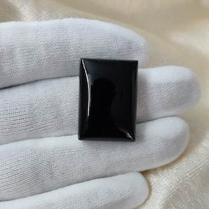 Könnte beinhalten: Ein schwarzer rechteckiger Edelstein mit einer glatten, polierten Oberfläche.