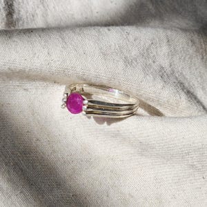 May include: A silver ring with a pink gemstone set in the center. The ring has a simple, elegant design and is perfect for everyday wear.