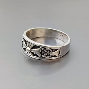 May include: A silver ring with a cross design. The cross has a small, round, gold center.