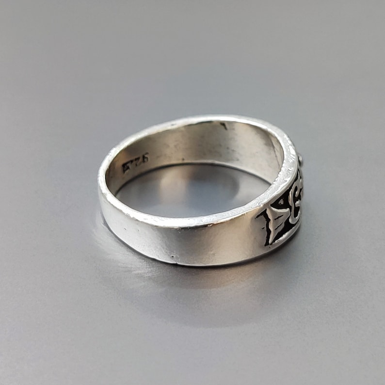 May include: A silver ring with a detailed design on the band. The ring is marked with the number "925" on the inside.