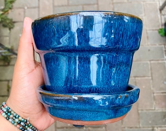 May include: A deep blue ceramic planter with a glazed finish. The planter has a wide rim and a slightly flared base.
