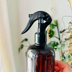 Puede incluir: Una botella de spray de vidrio marr&oacute;n con un pulverizador de gatillo negro. La botella est&aacute; parcialmente llena de un l&iacute;quido transparente.