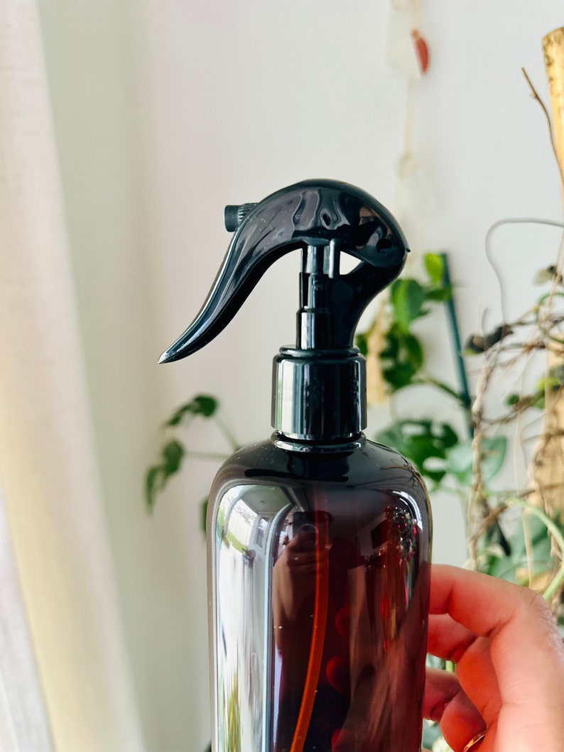 Puede incluir: Una botella de spray de vidrio marr&oacute;n con un pulverizador de gatillo negro. La botella est&aacute; parcialmente llena de un l&iacute;quido transparente.