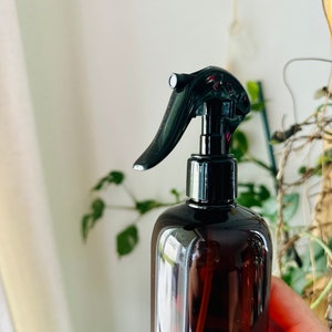 Puede incluir: Una botella de spray de vidrio marr&oacute;n con un pulverizador de gatillo negro. La botella est&aacute; parcialmente llena de un l&iacute;quido transparente.
