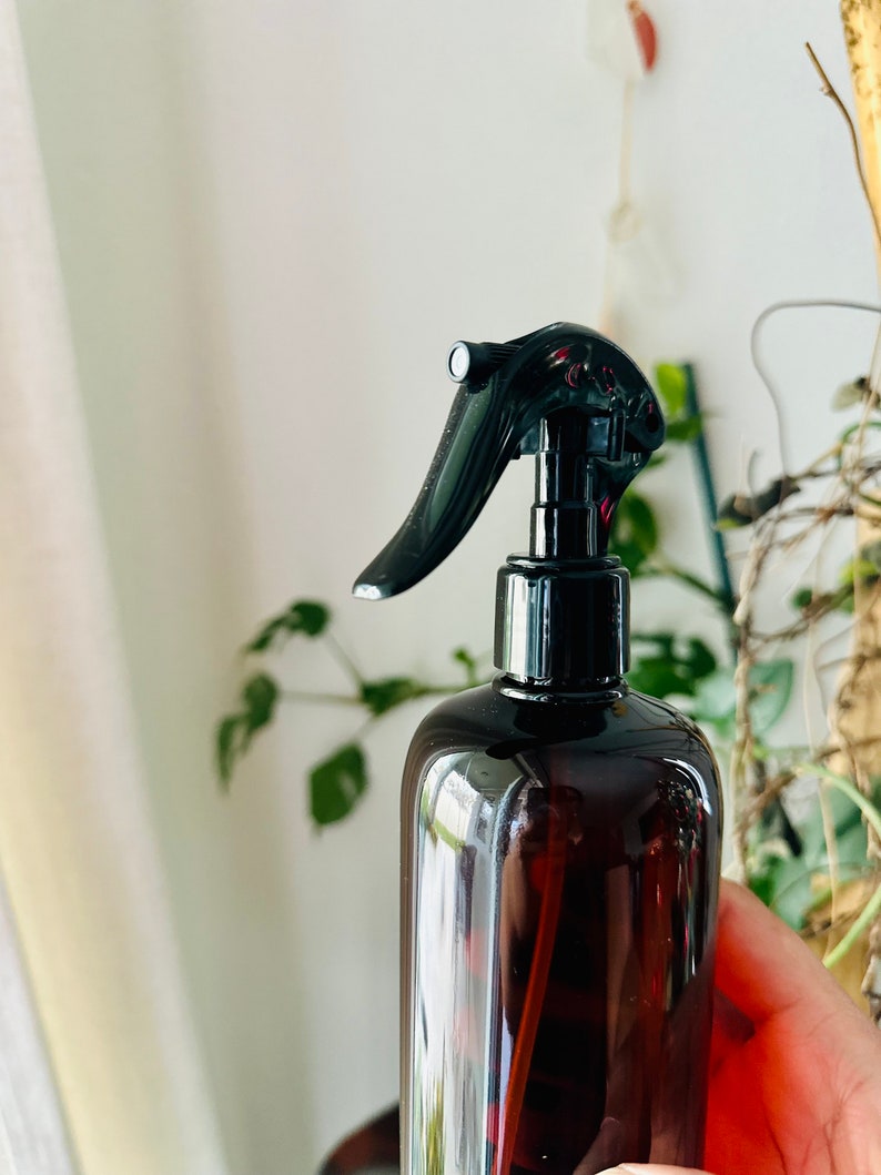 Puede incluir: Una botella de spray de vidrio marr&oacute;n con un pulverizador de gatillo negro. La botella est&aacute; parcialmente llena de un l&iacute;quido transparente.