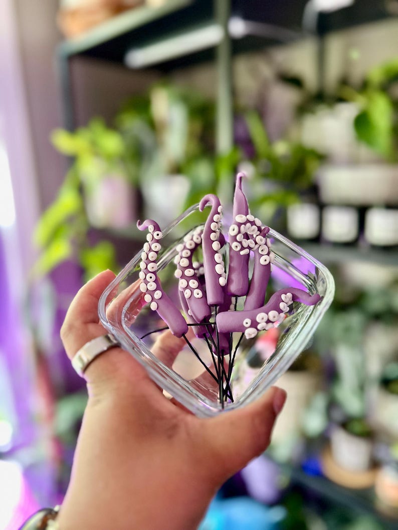 May include: A glass container filled with purple octopus tentacles with white suction cups. The tentacles are arranged in a bouquet-like shape.