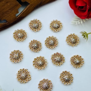 May include: A collection of twelve circular gold-toned buttons, each featuring a radiating sunburst pattern with a small, clear, central rhinestone accent. The buttons have a scalloped outer edge and a metallic finish, arranged in a loose cluster.