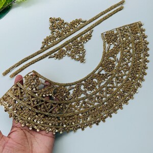 以下が含まれることがあります： 金色の刺繍レーストリム。花柄と幾何学模様が施されています。トリムには、曲線のネックラインピース、2つのストレートピース、小さな花のアクセントが含まれています。トリムはスパンコールとビーズで装飾されています。