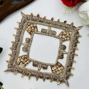 May include: A square-shaped gold embroidered patch featuring intricate metallic thread work, small circular sequins, and bead accents. The border is detailed with textured gold stitching and dangling sequin elements along the outer edges.