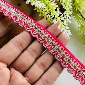 Op de afbeelding: Een felroze decoratieve bies met een geschulpte rand en gedetailleerd zilver borduurwerk. De bies heeft kleine, ronde versieringen langs de rand, wat een vleugje elegantie toevoegt. Ideaal voor het verfraaien van kleding, accessoires of woondecoratieprojecten.