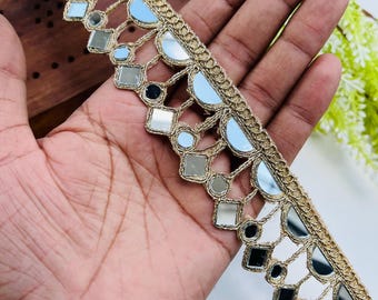 Può includere: Bordura decorativa dorata con dettagli a specchio. La bordura presenta un motivo ripetuto di semicerchi e quadrati, ciascuno contenente piccoli specchi. La bordura è tenuta in mano, evidenziando il suo design intricato e le proprietà riflettenti.