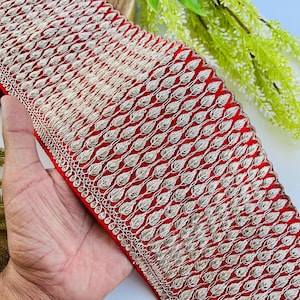 Puede incluir: Un ribete de tela roja vibrante con un intrincado patrón de hojas doradas. El ribete presenta un diseño detallado con un borde festoneado, perfecto para adornar prendas o manualidades. El hilo dorado crea un hermoso contraste.