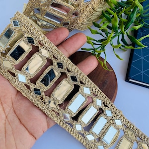 May include: Gold trim lace with rectangular mirror embellishments. The lace is a light beige color and the mirrors are clear.