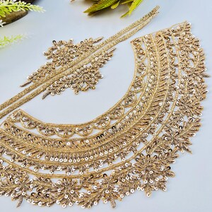 May include: Gold-coloured embroidered lace trim and appliques. The trim features detailed floral and leaf patterns, and is embellished with sequins. The appliques have a similar design. These items are likely for embellishing clothing or accessories.