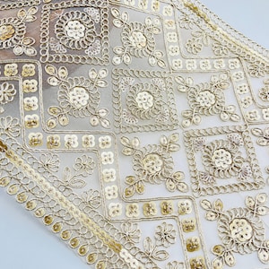 Op de afbeelding: Close-up van een gouden tafelloper met een herhalend patroon van bloem- en geometrische vormen, versierd met pailletten. De transparante stof heeft een delicate, kantachtige textuur. Ideaal voor speciale gelegenheden.