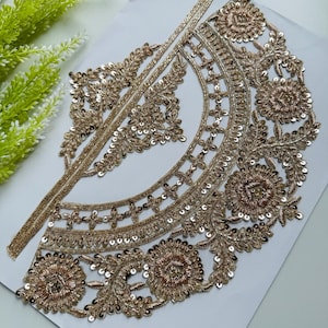 Op de afbeelding: Een gedetailleerde, goudkleurige geborduurde applicatie met bloemen- en geometrische patronen. De applicatie heeft ingewikkeld kralenwerk en pailletten, waardoor een glinsterend effect ontstaat. Het ontwerp is waarschijnlijk bedoeld voor het verfraaien van kleding of accessoires.