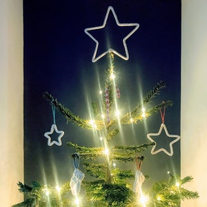 May include: A decorated Christmas tree with white star ornaments, candy cane decorations, and small white knitted stocking ornaments. The tree is lit with warm white lights, creating a festive holiday display.