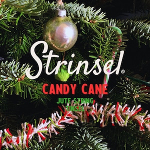 May include: A Christmas tree decorated with a red and white candy cane, white and red tinsel, and a silver bauble. The tree is decorated with a sign that reads "Strinsel Candy Cane Jute String Tinsel".
