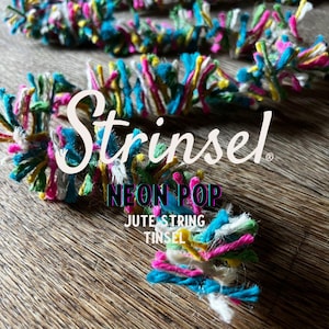 May include: Close-up of colourful jute string tinsel with the text "Strinsel Neon Pop". The tinsel features vibrant hues of pink, blue, yellow, and green. The tinsel is made of jute string.