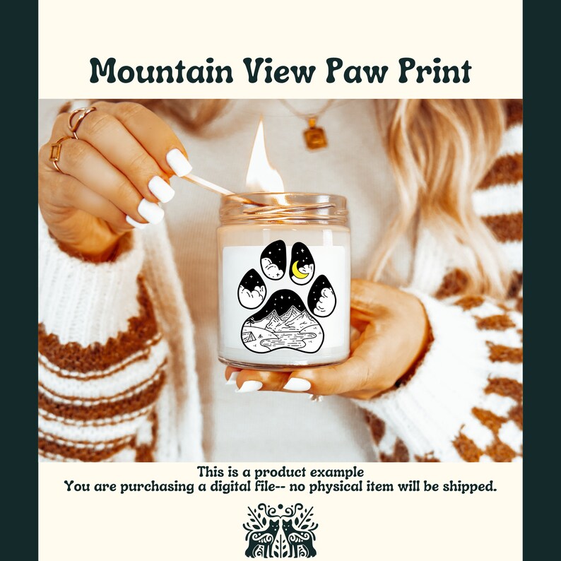 May include: A white candle with a black paw print design featuring a mountain scene, a crescent moon, and stars. The candle is lit and being held by a hand.