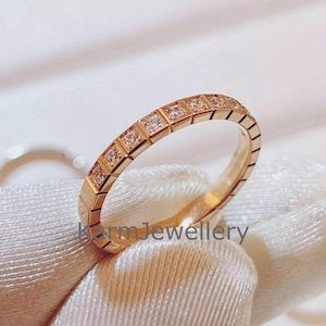 Op de afbeelding: Een gouden ring met een rij kleine vierkante diamanten die in de band zijn gezet.