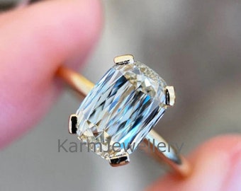 May include: A gold ring with a large, clear, rectangular-shaped gemstone. The ring is set with a bezel setting and has a polished finish.