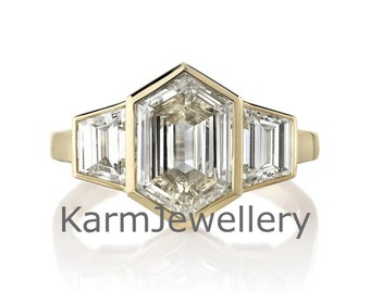 May include: A gold ring with three clear, geometric-cut gemstones. The center stone is a hexagonal shape, flanked by two rectangular stones. The ring has the text "KarmJewellery" at the bottom.