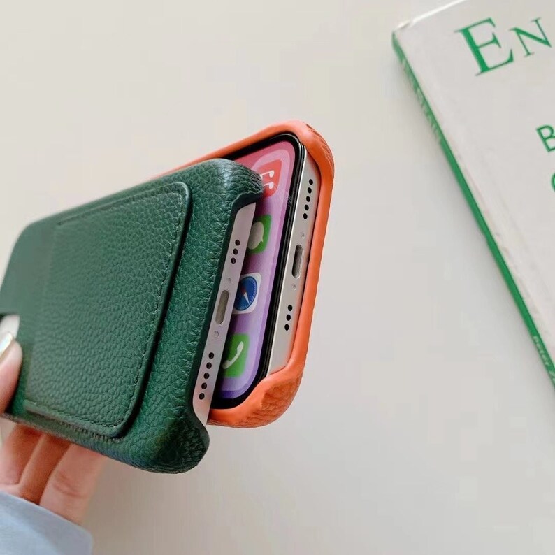 May include: A green leather phone case with a built-in card holder. The case is shown with a phone inside, and the phone has a bright orange case.