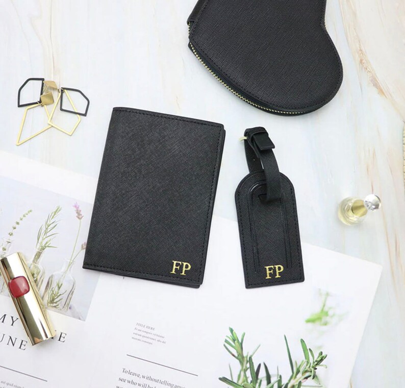 May include: A set of black leather travel accessories with gold initials "FP". The set includes a passport holder, a luggage tag, and a heart-shaped cosmetic bag.