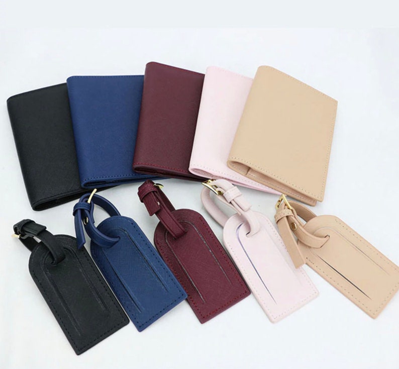 May include: Set of six leather luggage tags in various colors, including black, navy blue, burgundy, pink, beige, and brown. Each tag has a gold metal loop and a leather strap.