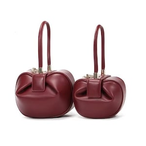 May include: Two burgundy leather handbags with a unique rounded shape and gold hardware. The handbags have top handles and a slightly puffed design.