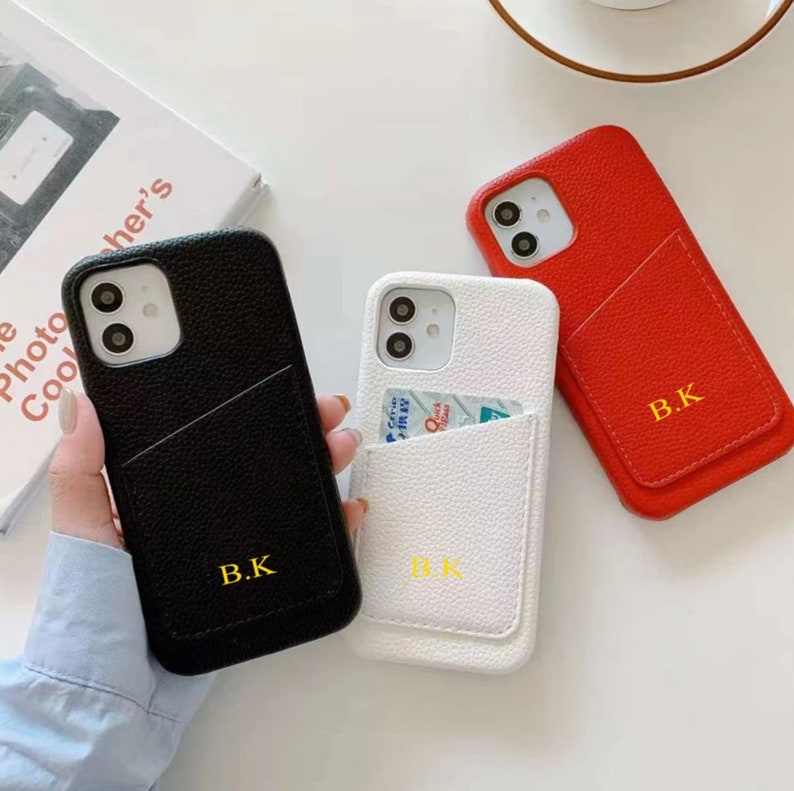 May include: Three phone cases with a pocket for a card. The cases are black, white, and red. Each case has the initials "B.K." printed on the back.