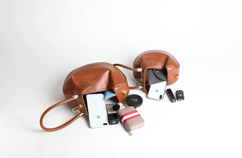 May include: Two brown leather handbags with gold hardware are open and filled with various items, including phones, wallets, and makeup.