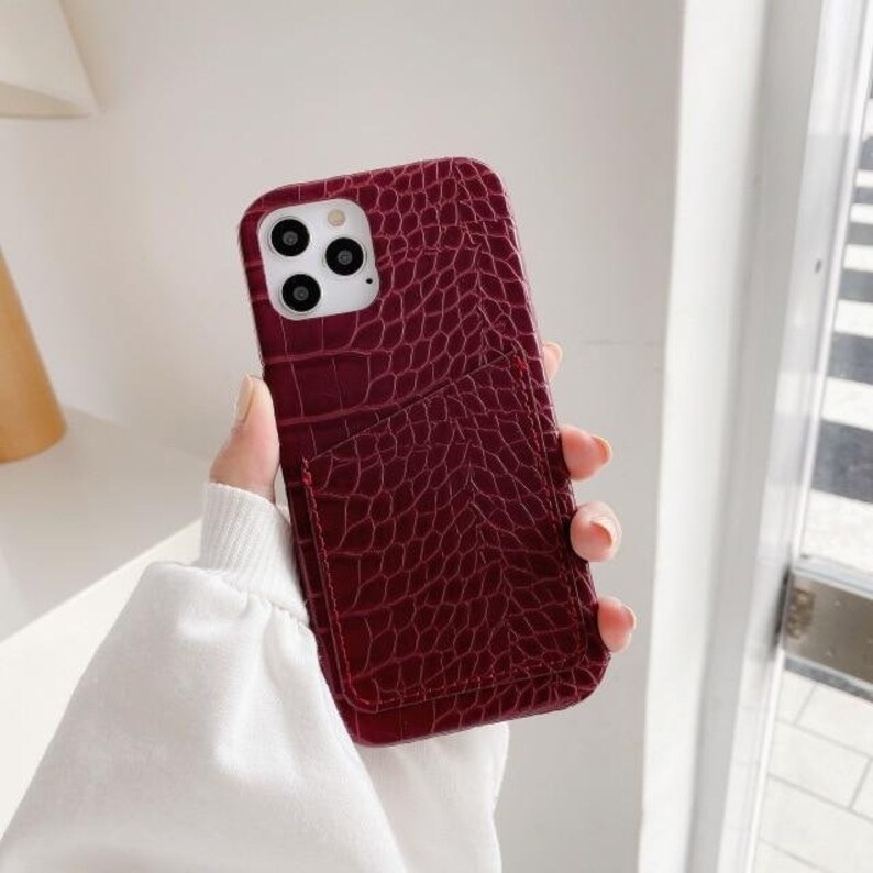 May include: A burgundy faux leather phone case with a crocodile pattern and a built-in card slot.