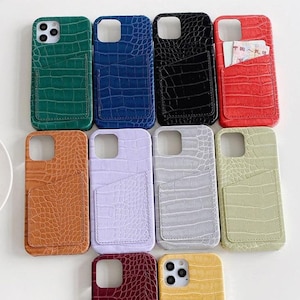 May include: Ten different colored phone cases with a crocodile skin pattern and a pocket on the back. The cases are in the following colors: green, blue, black, red, brown, purple, gray, light green, burgundy, and yellow.