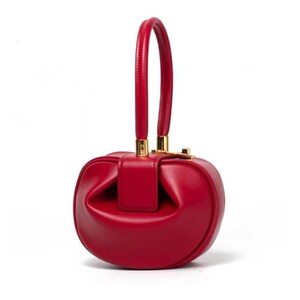 K&ouml;nnte beinhalten: Eine rote Ledertasche mit einem goldenen Henkel oben und einer abgerundeten, leicht abgeflachten Form.