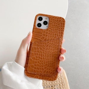 May include: A brown leather phone case with a crocodile pattern and a built-in card slot.
