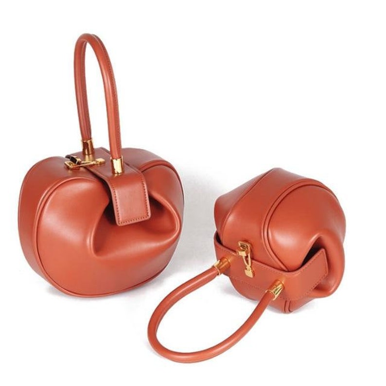 K&ouml;nnte beinhalten: Zwei braune Ledertaschen mit goldenen Beschl&auml;gen. Die gr&ouml;&szlig;ere Tasche hat einen oberen Griff und die kleinere Tasche hat einen oberen Griff und einen Schultergurt.